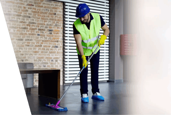 Worker performing after builders cleaning Dunedin, wearing safety gear and mopping a tiled floor in a newly constructed or renovated space.